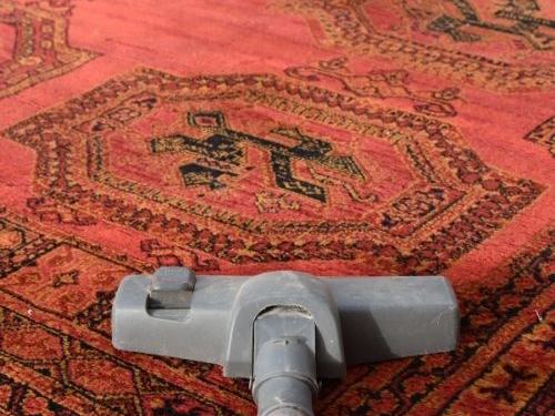 Red Persian-style rug being vacuumed before cleaning