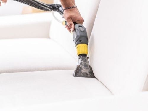 White fabric couch being cleaned with an upholstery extraction tool